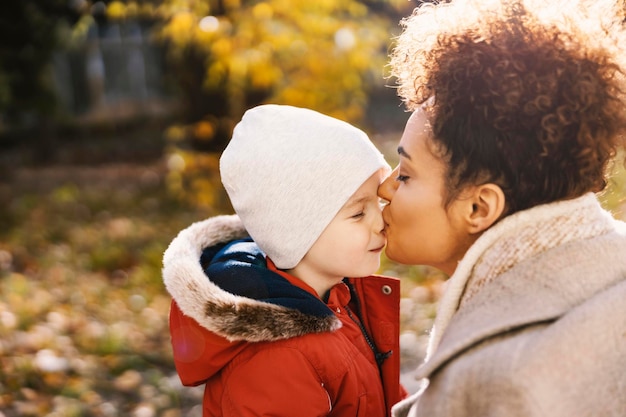 Photo caring caregiver kissing kindergarten child on the nose outdoors