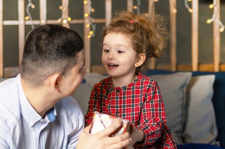 Caring dad making a surprise to child. Father giving his smiling daughter a gift box for a holiday at home.