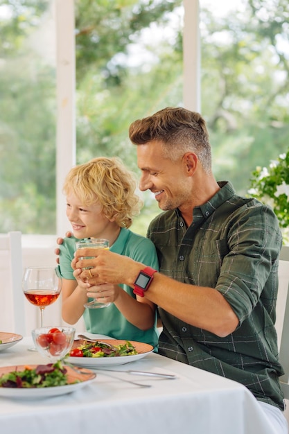 Caring daddy wearing smart watch giving his son glass of lemonade