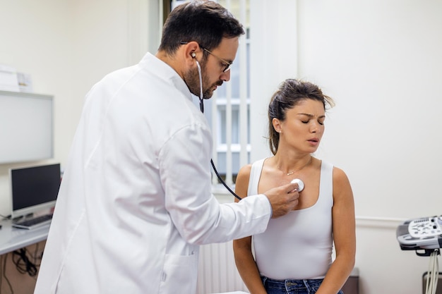 Caring doctor hold stethoscope listen to patient heart chest in\
hospital young woman do checkup examination in clinic healthcare\
concept