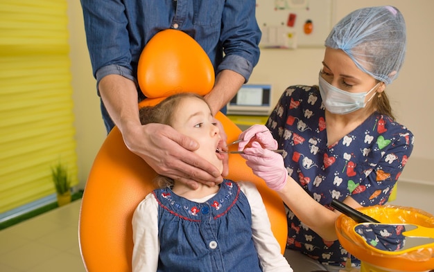 A caring father calms his little daughter during dental treatment in dentistry the father holds