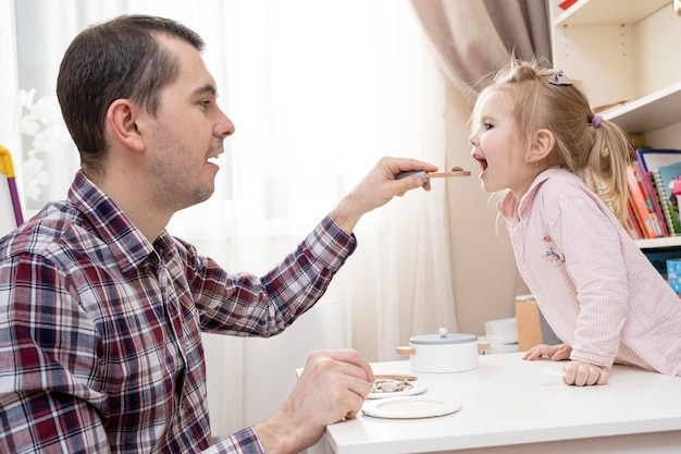 愛する娘にスプーンでおいしい食べ物を与える思いやりのある父親