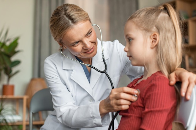Caring female cardiologist holding stethoscope and listening to girl kid patient at consultation