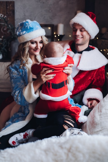 Caring mother in blue coat sitting beside her husband and baby both dressed in Santa costumes. Holiday concept