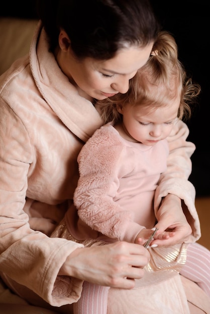 Caring mother cutting daughter's nails at home