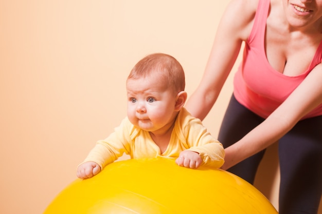 Caring mother doing sport exercises with her baby on fitball