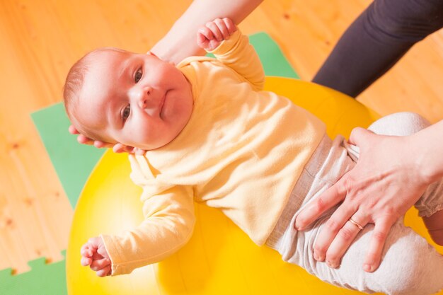 Caring mother doing sport exercises with her baby on fitball