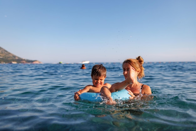 Caring mother rides her son on an inflatable ring in the sea