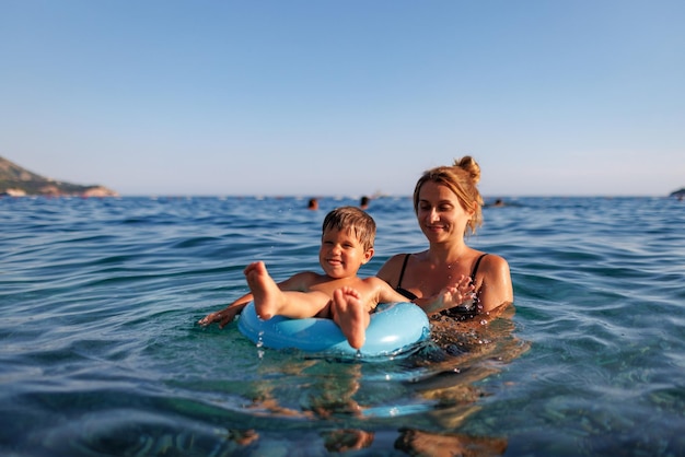 Caring mother rides her son on an inflatable ring in the sea