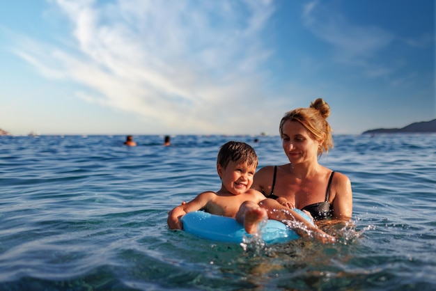 Caring mother rides her son on an inflatable ring in the sea