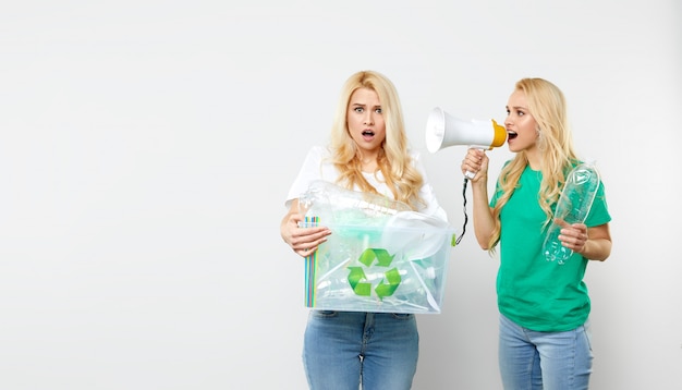 자연을 돌보는 것. 녹색 티셔츠에 확성기와 젊은 미국 여성 플라스틱 병 및 폐기물 상자를 들고있다. 자원 봉사자들은 쓰레기를 모아서 재활용했습니다.