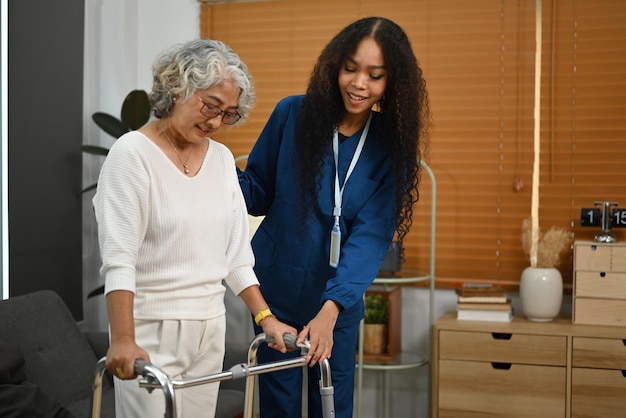 Photo caring nurse attending helping elderly woman walking frame walker at home home health care service concept