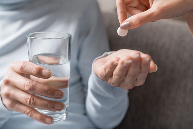 Caring nurse giving pills to senior woman with glass of water in hand