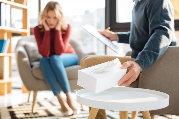 Caring psychologist. Selective focus of a box with paper tissues being taken by a smart male psychologist