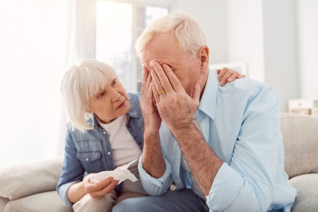 Caring wife. Petite senior woman holding a tissue and stroking her husbands back, trying to console him, while he crying