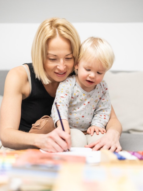 Photo caring young caucasian mother and small son drawing painting in notebook at home together loving mom