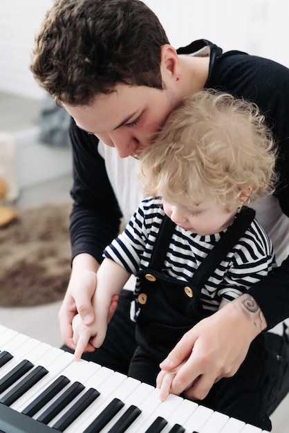 Caring young dad teaches his little curly child son to play the piano