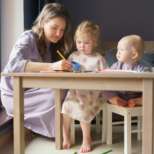 Caring young mom teaching how to draw her two little kids