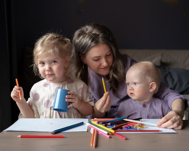 Заботливая молодая мама учит рисовать двух своих маленьких детей