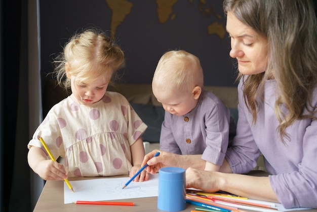 Фото Заботливая молодая мама учит рисовать двух своих маленьких детей