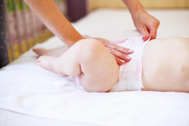 Caring young mother changing the diaper of her baby at home