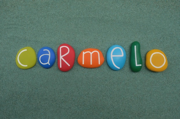 Foto carmelo mannelijke voornaam samengesteld met veelkleurige stenen letters over groen zand