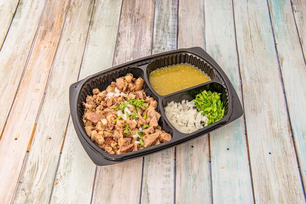 Photo carnitas menu tray with white onion cilantro and nopales sauce in home delivery container on wooden table