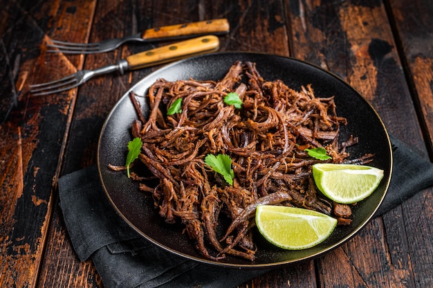 Carnitas in a plate with celery and lime wedges Wooden background Top view