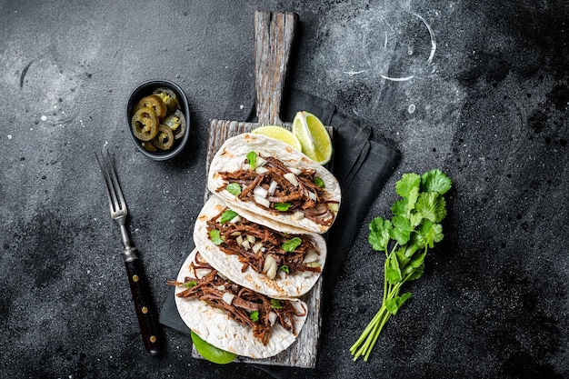 Carnitas-taco's van varkensvlees op maïstortilla's met ui en limoen Zwarte achtergrond Bovenaanzicht