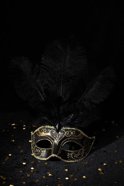 Foto maschera d'oro di carnevale con piume e confetti su sfondo nero