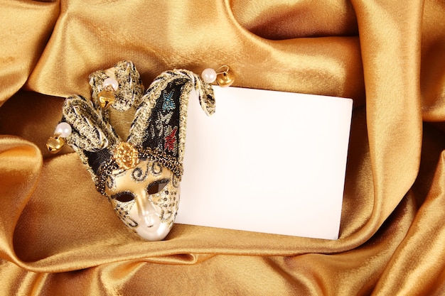 Carnival mask lying on a yellow silk and a sheet of white paper