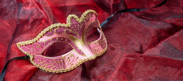 Carnival venetian pink mask on red color fabric background female disguise masquerade