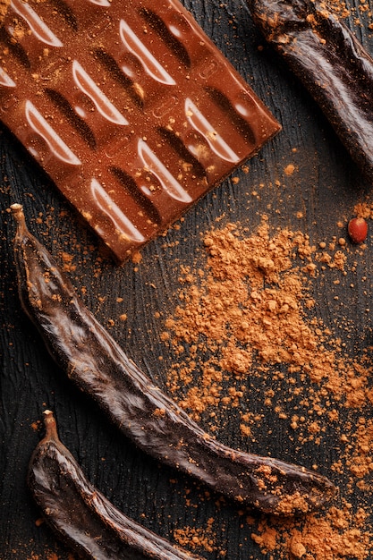 Carob chocolate and carob fruit powder on dark surface
