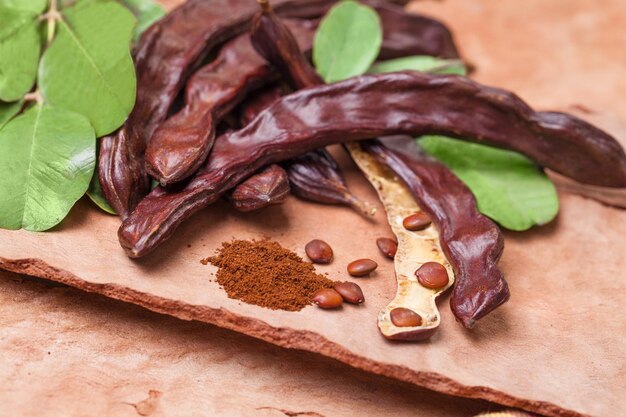 Photo carob organic carob pods with seeds and leaves on tree bark table healthy eating food background