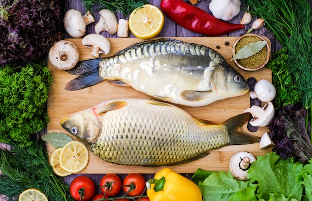 Carpa e carpa a specchio su un tagliere circondato da verdure. pesce fresco prima della cottura con verdure