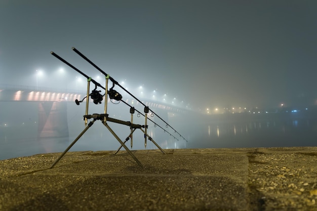 Carp spinning reel angling rods in foggy night. Urban Edition. Night Fishing, Carp Rods, City lights. Foggy night.