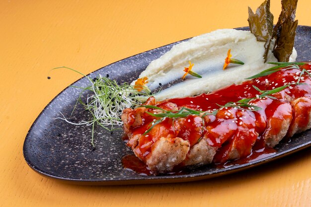 Carp in sweet and sour Chinese sauce with mashed potatoes and grape leaves On a dark ceramic platter