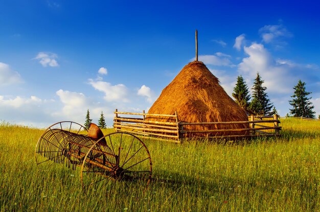 Carpathian mountains summer landscape with blue sky, clouds, haystack and old rusty agricultural instrument, natural summer background