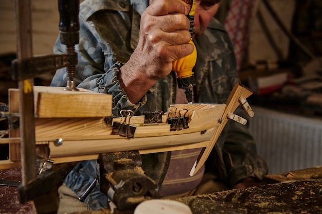 Carpenter in action, lifestyles, hobby concepts. Craftsman sticking wooden details on a sailboat in his own workshop.