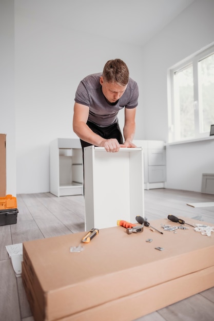 Фото Плотник, собирающий мебель, портрет работника, собирающего кухонный ящик с полным набором инструментов