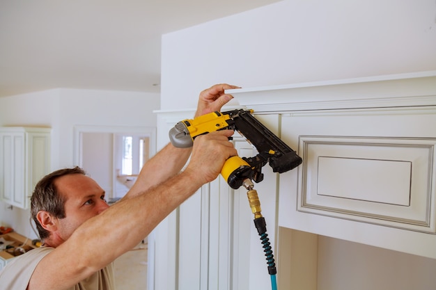 Carpenter brad utilizzando la pistola sparachiodi a crown molding su mobili da cucina che incorniciano finiture,