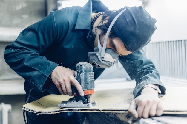 A carpenter cuts a board with an electric jigsaw. manufacture of skateboards.