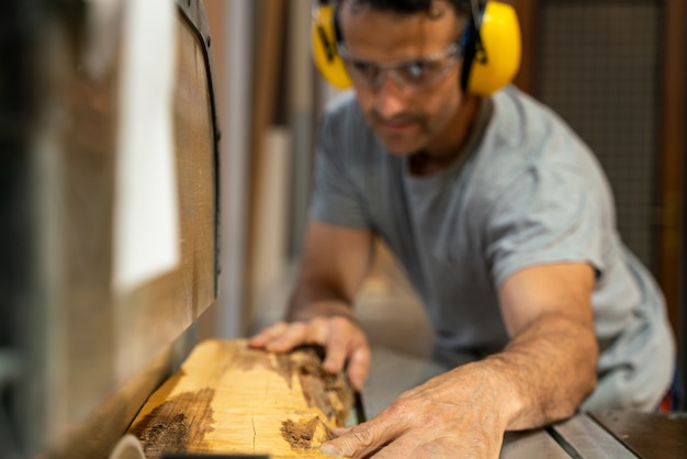 Carpenter cutting wood with a machine wearing earplugs. 