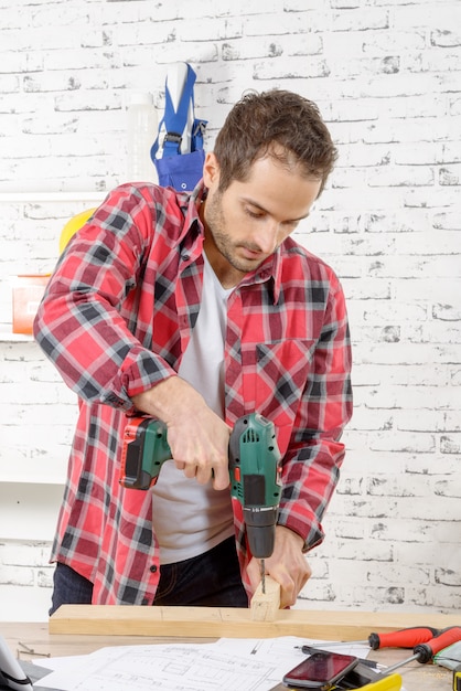 Carpenter drilling hole in plank, in his workshop