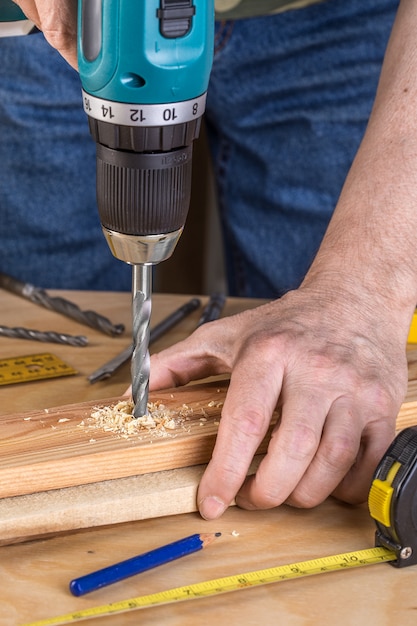 Carpentiere che perfora legno usando la perforatrice portatile