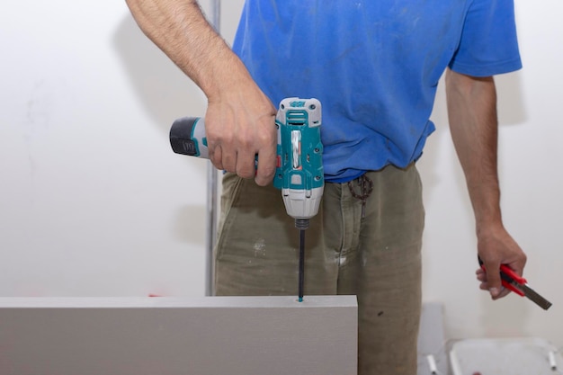 A carpenter drills a hole in a wooden board with an electric drill