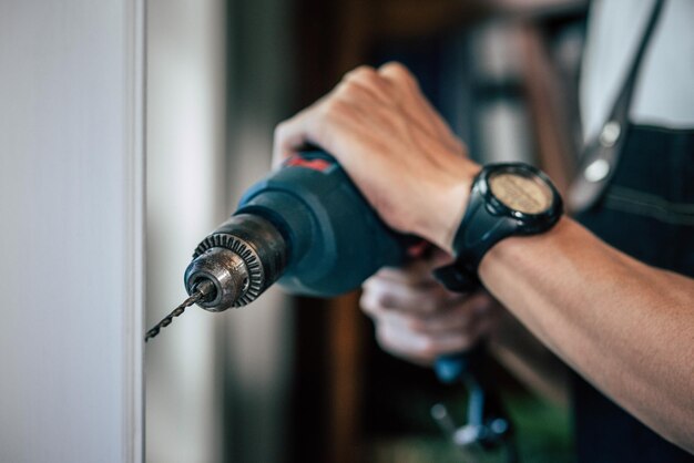 The carpenter holds the drill and drills the window