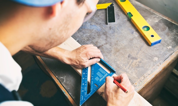 The carpenter is draw the line by pencil on the wooden plank