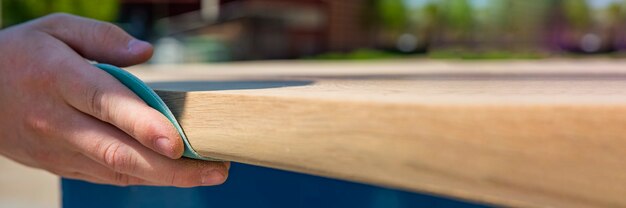 A carpenter is grinding a wooden board with sandpaper. The process of making wooden furniture. Hands of the master close-up.