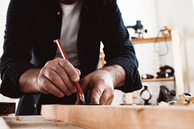 Carpenter makes pencil marks on a wood plank